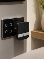 Indoor chime unit of the Lavora Sentinel plugged into a wall socket beside a light switch panel